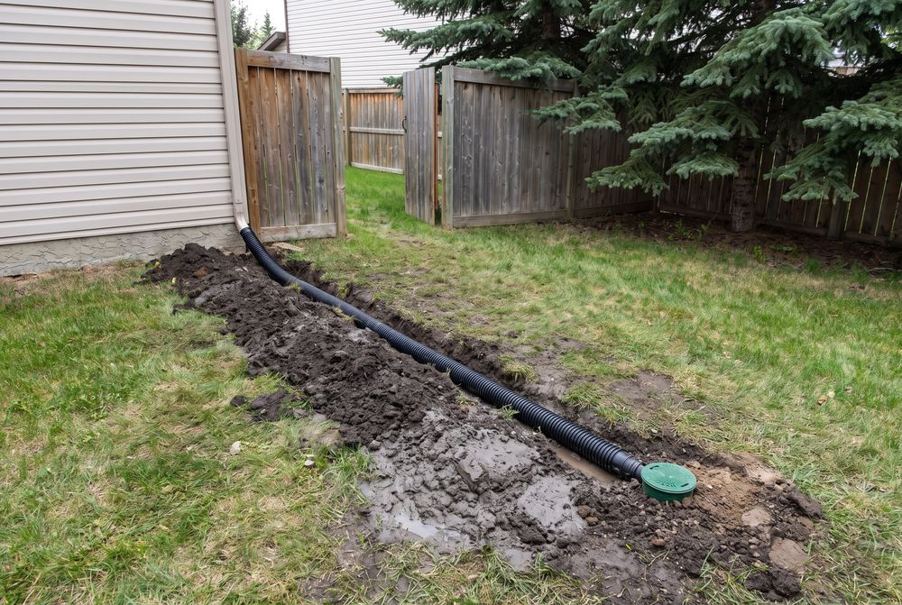 Corrugated drain pipe in a shallow trench from a downspout to a pop-up emitter