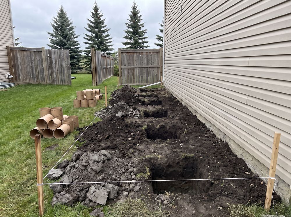 Line of square deck footing holes with sonotube forms stacked nearby