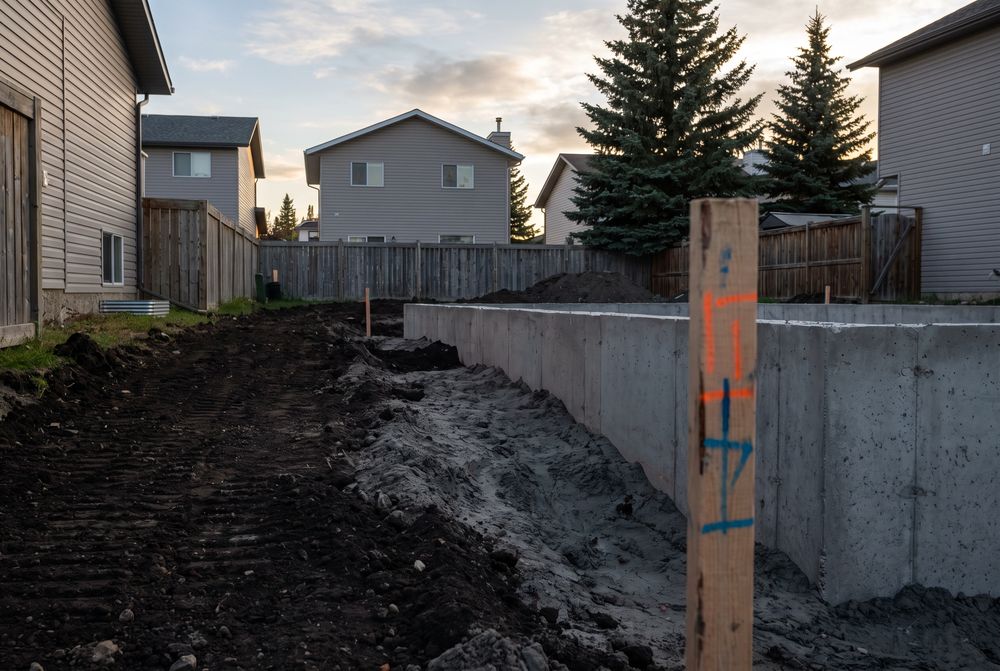 Fresh clay graded to slope away from a new concrete foundation with a grade stake