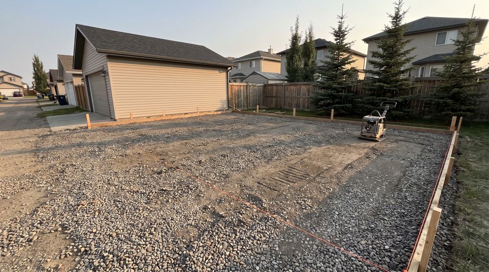 Crushed gravel being spread and levelled for a parking pad beside a garage