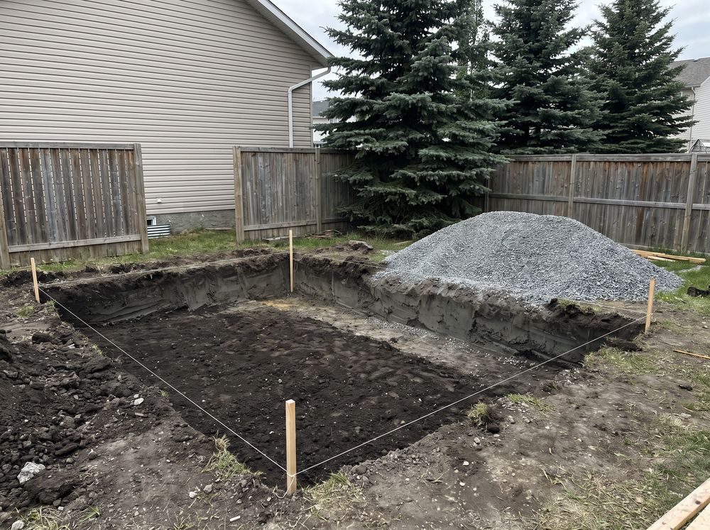 Rectangular patio base excavation with string lines and a gravel pile ready to spread