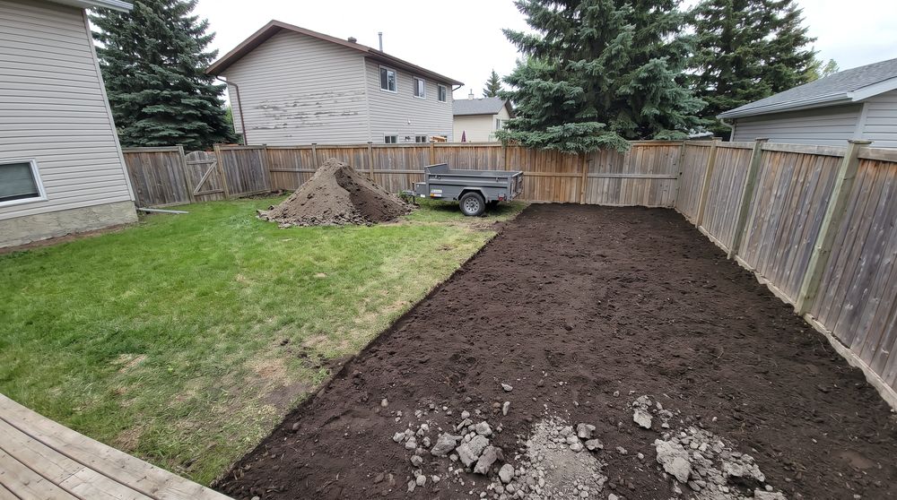 Half a backyard lawn stripped to dark topsoil with a dump trailer at the fence