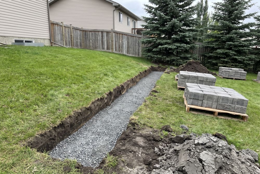 Gravel-based footing trench for a retaining wall with pallets of blocks stacked nearby