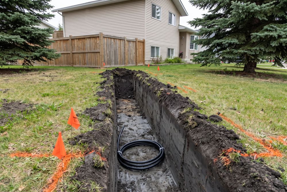 Narrow straight trench across a lawn with a black poly water line and orange locate flags